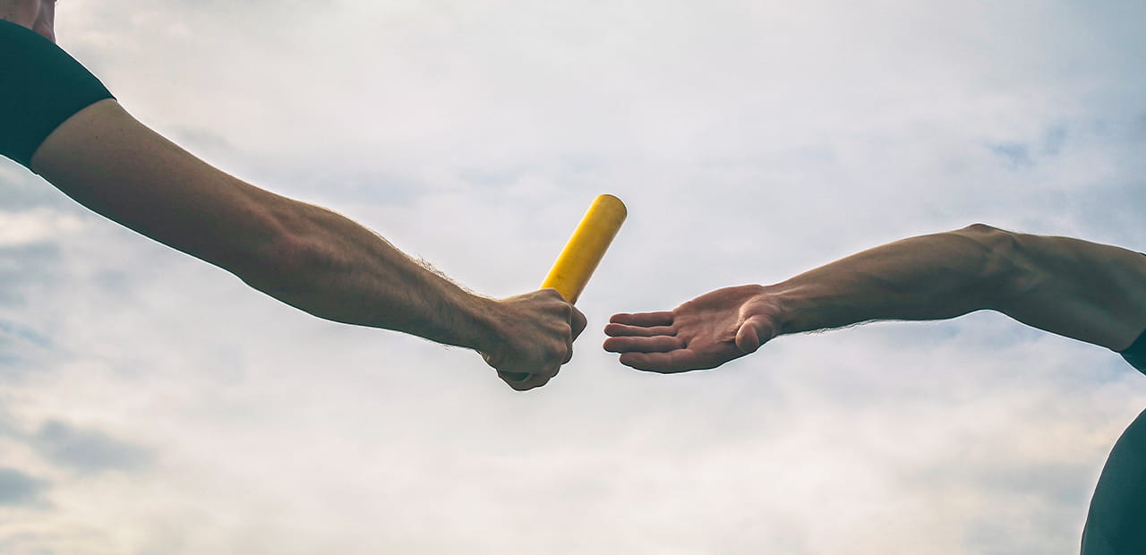 Two people pass a relay baton during a race, symbolizing how board leadership creates lasting impact by sharing responsibility, guiding mission-driven work and strengthening communities for future generations.