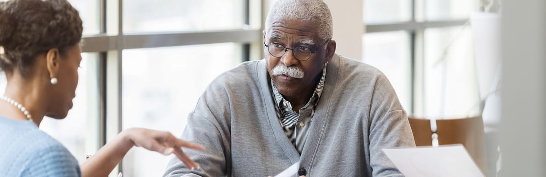 Elderly man sits across from a female professional holding a document.