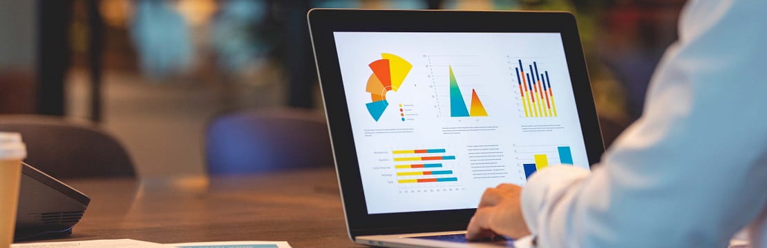 Man sits at a table and types on a computer, which is displaying different charts and graphs