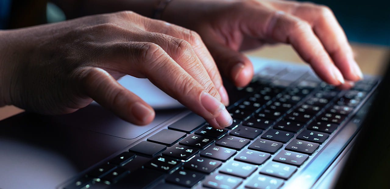 Hands typing on a laptop, illustrating the growing threat of AI-powered impersonation scams. 
