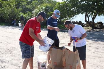 Men dump buckets of trash into paper waste bags