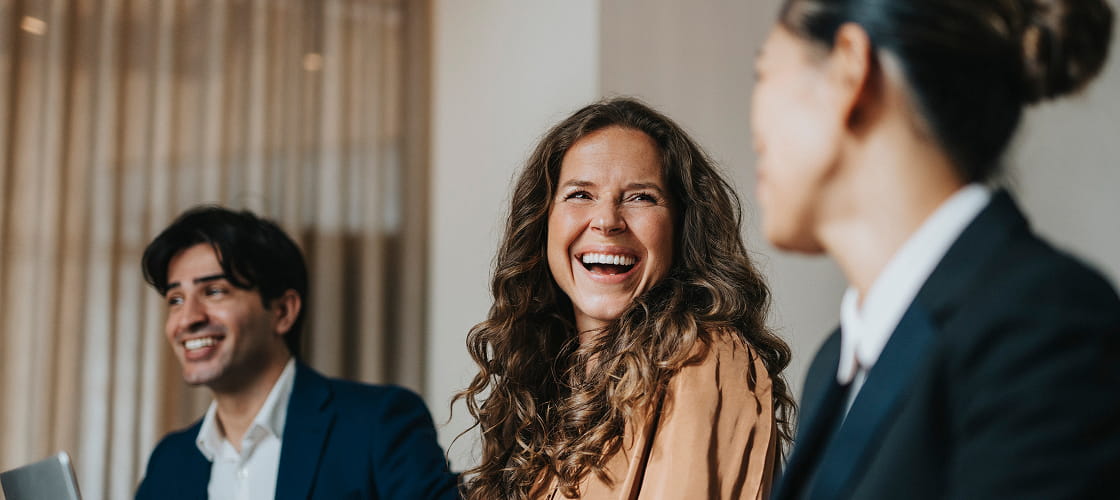 Happy mature businesswoman sitting amidst male and female colleague at office