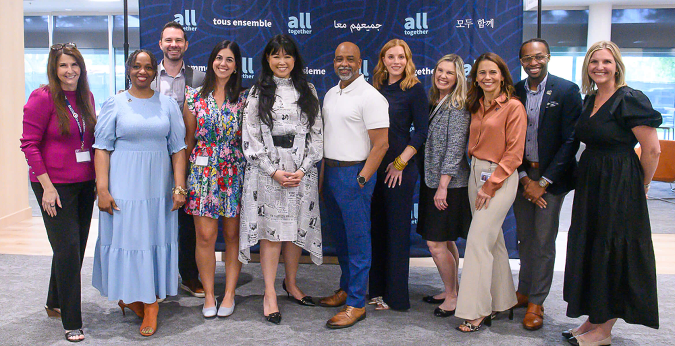 Group of employees posing together in front of an All Together event backdrop during a company inclusion and employee engagement event.