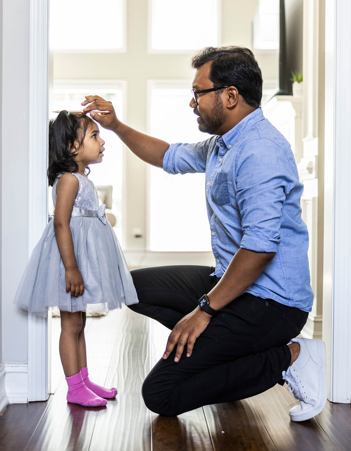Father measuring toddlers daughter's height against wall at home